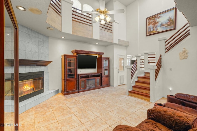 living room with stairs, light tile patterned floors, a tiled fireplace, and a ceiling fan