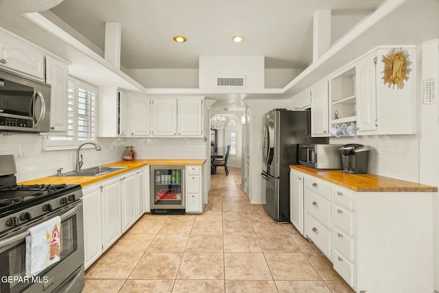 kitchen with light tile patterned floors, appliances with stainless steel finishes, a sink, butcher block countertops, and beverage cooler