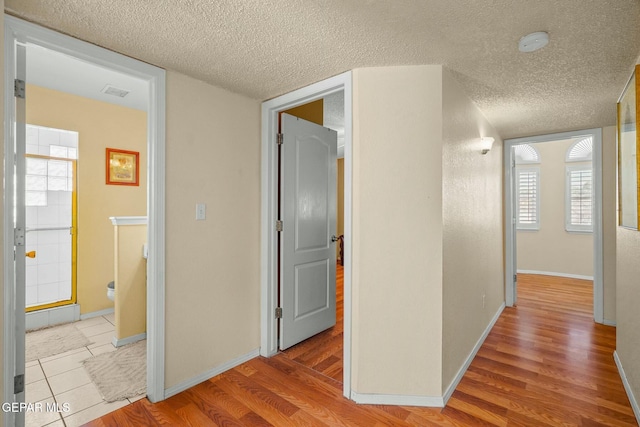 corridor with a textured ceiling, wood finished floors, visible vents, and baseboards