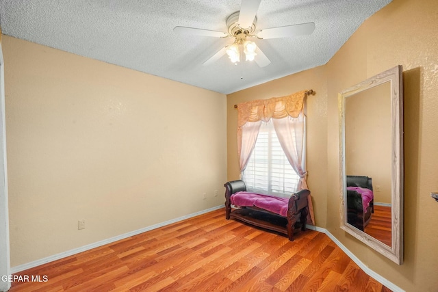 sitting room featuring a ceiling fan, baseboards, a textured ceiling, and light wood finished floors