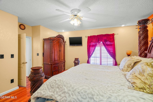 bedroom with ceiling fan, a textured ceiling, baseboards, and wood finished floors