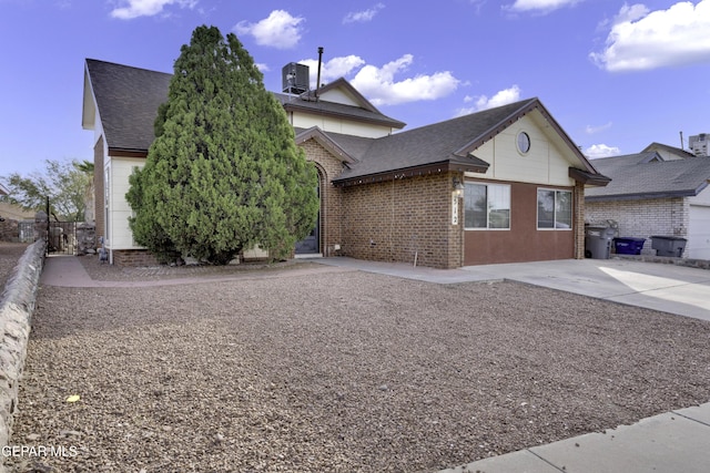 view of property exterior with a shingled roof, brick siding, fence, and central AC