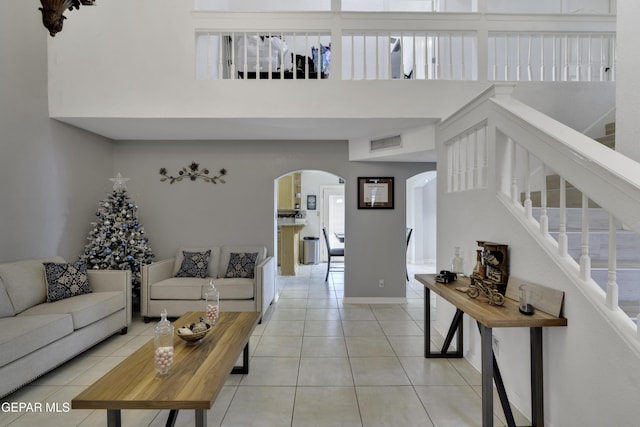 tiled living area featuring baseboards, visible vents, arched walkways, stairway, and a high ceiling