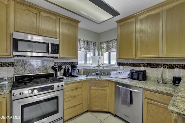 kitchen featuring appliances with stainless steel finishes, a sink, decorative backsplash, and light tile patterned floors