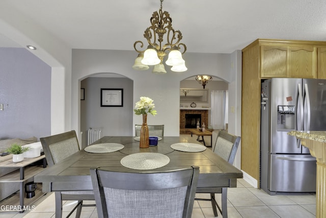 dining room featuring arched walkways, light tile patterned flooring, a fireplace, and a notable chandelier