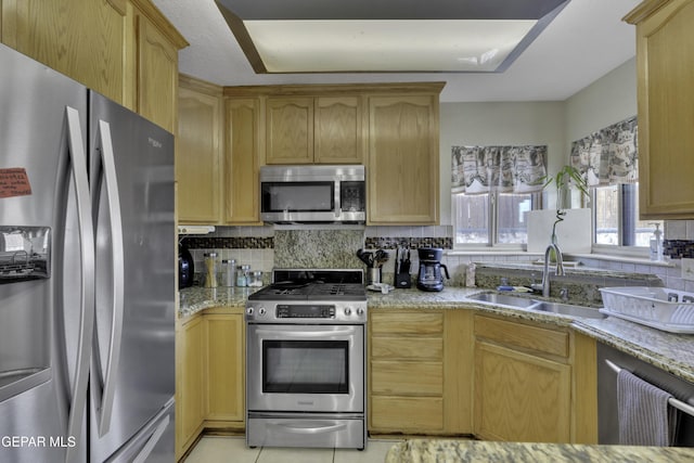 kitchen with stainless steel appliances, backsplash, a sink, and light stone countertops