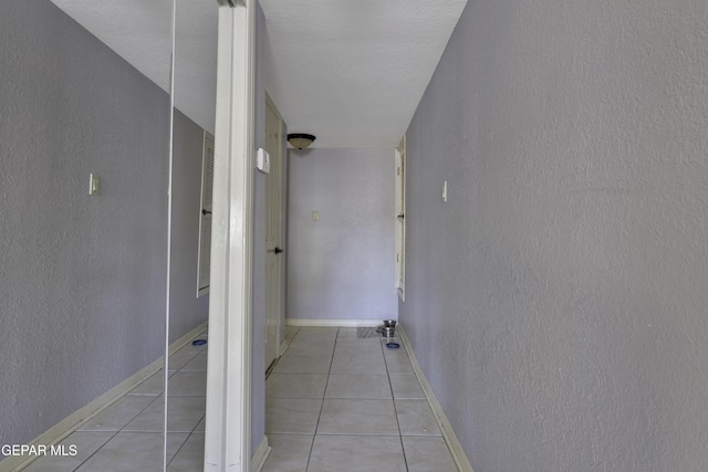 hallway featuring light tile patterned floors, a textured wall, and baseboards