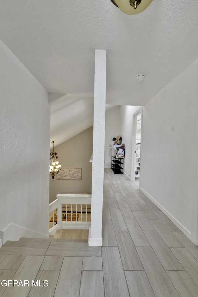 hall with decorative columns, baseboards, lofted ceiling, wood tiled floor, and a notable chandelier