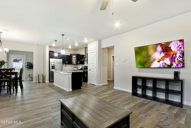 kitchen featuring light countertops, an island with sink, wood finished floors, stainless steel fridge, and range