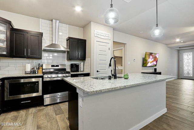 kitchen with wall chimney exhaust hood, stainless steel gas range, built in microwave, light wood-style floors, and a sink