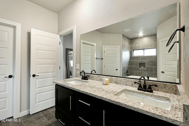 bathroom featuring tiled shower, a sink, baseboards, and double vanity