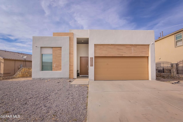 view of front of home with driveway, an attached garage, fence, and stucco siding