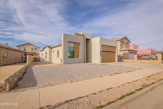 view of front of house with a garage, concrete driveway, fence, and stucco siding