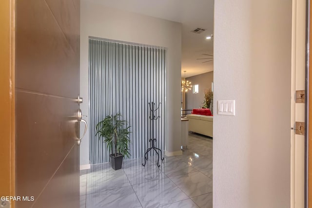 hallway with marble finish floor, visible vents, a notable chandelier, and baseboards