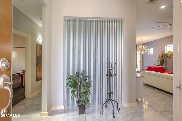 hall featuring a chandelier, baseboards, and tile patterned floors