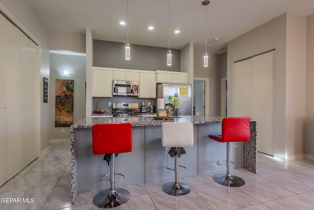 kitchen featuring a breakfast bar, a high ceiling, appliances with stainless steel finishes, stone countertops, and white cabinetry