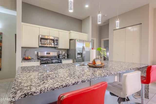 kitchen with light stone counters, appliances with stainless steel finishes, a breakfast bar, and white cabinets