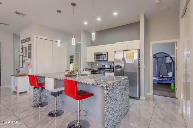 kitchen featuring marble finish floor, stainless steel appliances, white cabinets, a sink, and a kitchen breakfast bar