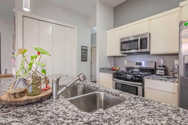 kitchen with appliances with stainless steel finishes, stone counters, and a sink