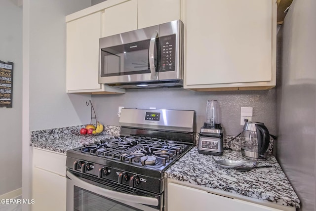 kitchen featuring stainless steel appliances, light stone countertops, and white cabinets