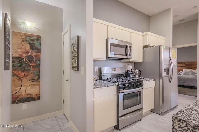 kitchen with light stone counters, marble finish floor, stainless steel appliances, white cabinets, and baseboards