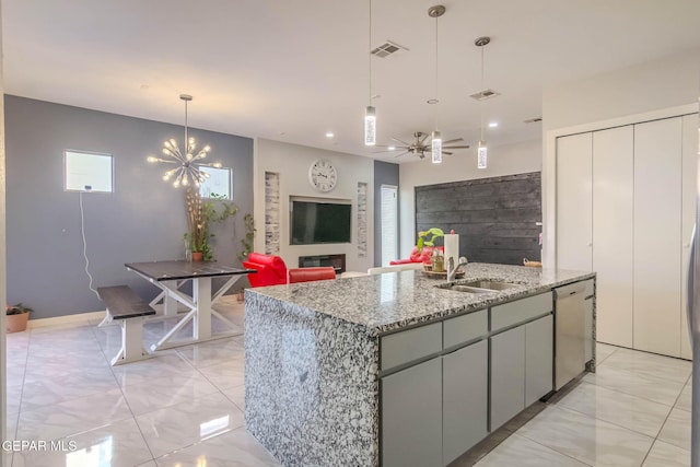 kitchen with an island with sink, light stone counters, decorative light fixtures, stainless steel dishwasher, and a sink