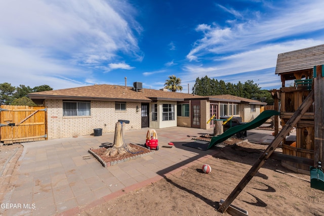 rear view of house with a shingled roof, fence, a patio area, a playground, and brick siding