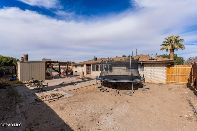 back of property featuring a trampoline, an outbuilding, brick siding, a patio area, and fence