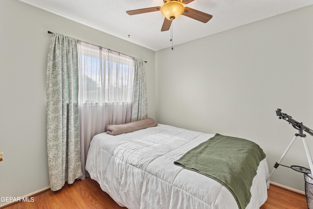 bedroom with ceiling fan, a textured ceiling, wood finished floors, and baseboards