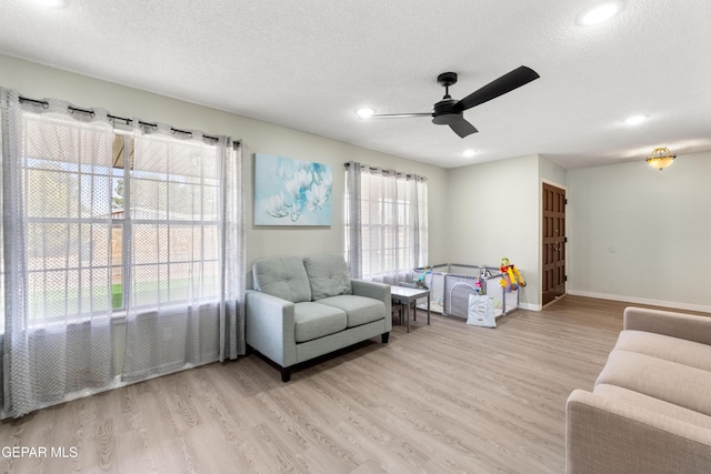 living area with a ceiling fan, light wood-style flooring, baseboards, and a textured ceiling