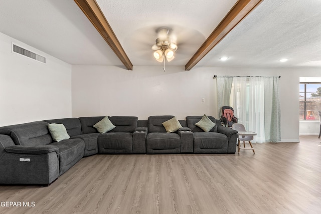 living area with light wood-style floors, a textured ceiling, visible vents, and beamed ceiling