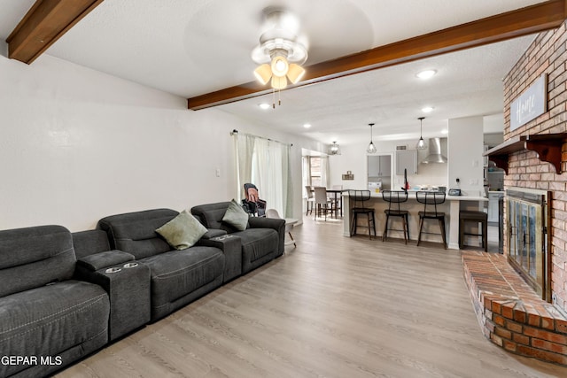 living room featuring light wood-style floors, a brick fireplace, and beamed ceiling