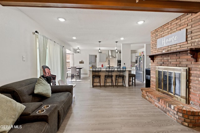 living room with light wood-style floors, a brick fireplace, a textured ceiling, and recessed lighting