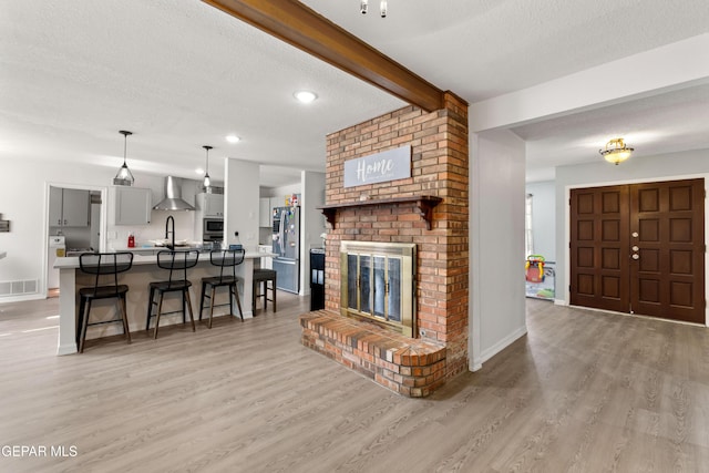 living room with light wood-style flooring, visible vents, beamed ceiling, and a textured ceiling