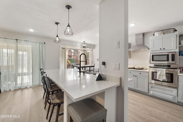 kitchen with light wood finished floors, stainless steel appliances, wall chimney range hood, and a textured ceiling