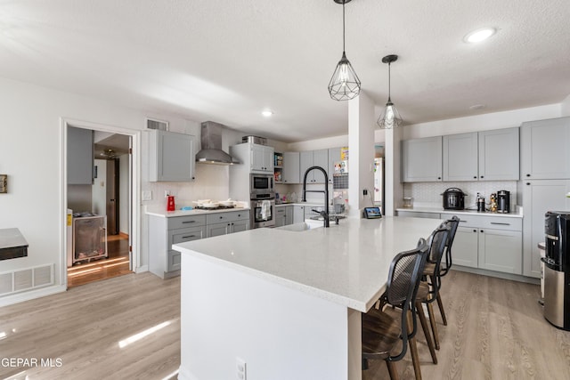 kitchen featuring stainless steel appliances, visible vents, wall chimney range hood, gray cabinets, and light wood finished floors