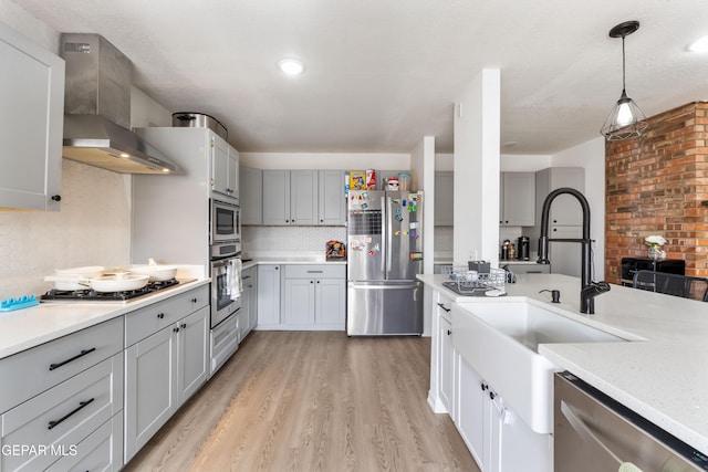 kitchen featuring light wood-style flooring, a sink, light countertops, appliances with stainless steel finishes, and wall chimney exhaust hood