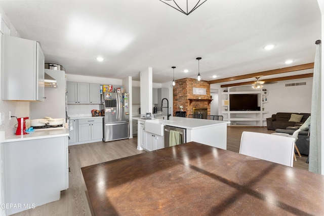 kitchen with a fireplace, a sink, visible vents, open floor plan, and appliances with stainless steel finishes