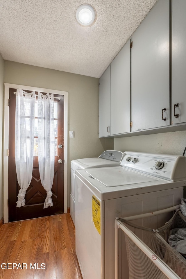 clothes washing area with a textured ceiling, light wood-style flooring, cabinet space, and washer and dryer