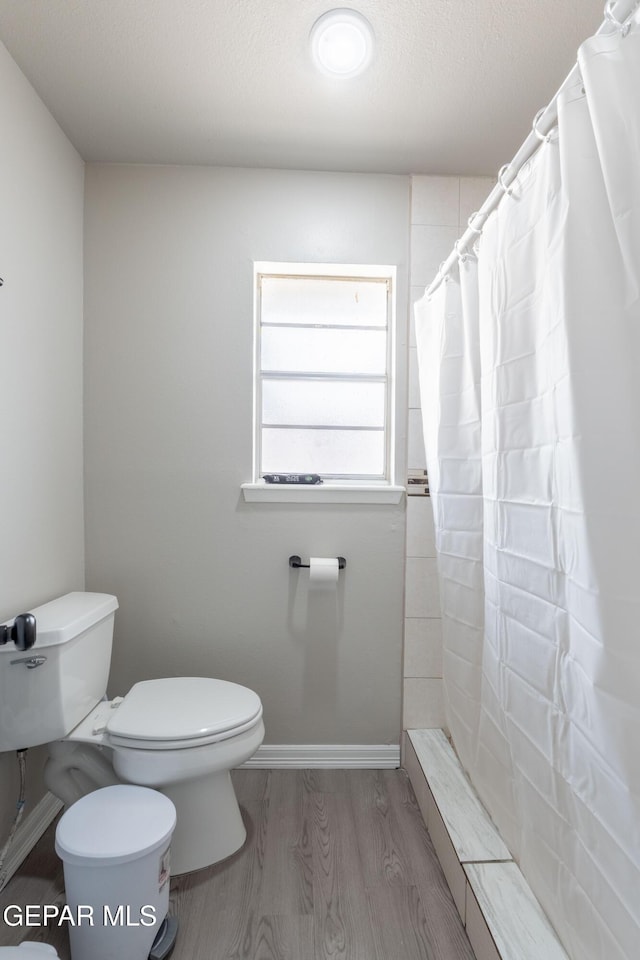 bathroom featuring toilet, a tile shower, a textured ceiling, wood finished floors, and baseboards