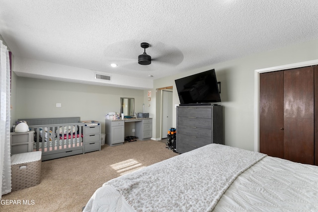 carpeted bedroom featuring multiple closets, visible vents, a textured ceiling, and a ceiling fan