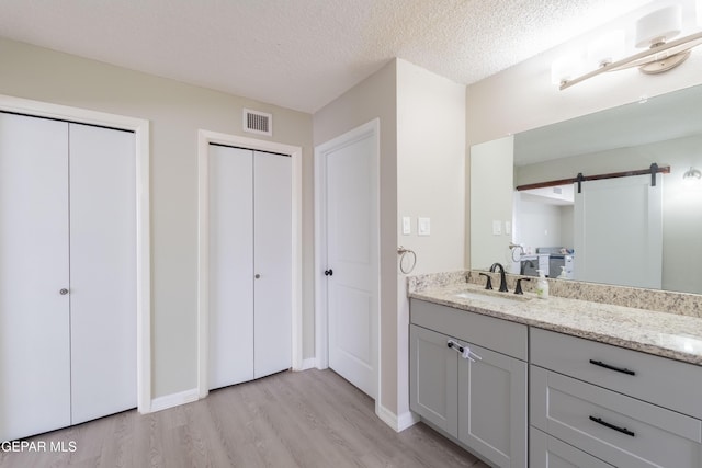 bathroom featuring a textured ceiling, wood finished floors, visible vents, vanity, and baseboards