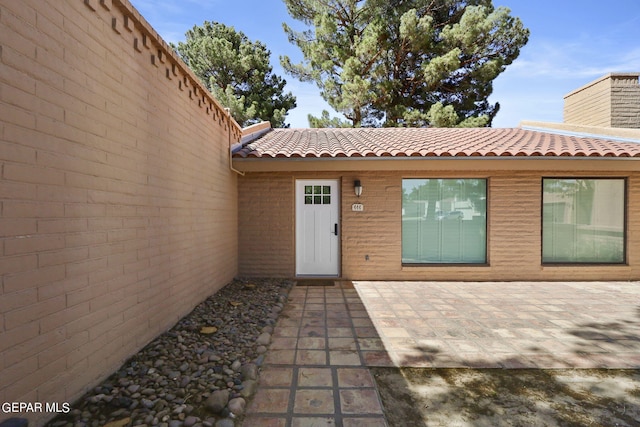 view of exterior entry with a tile roof, a patio, a chimney, and brick siding