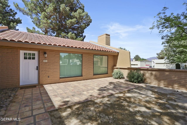 back of property with a tiled roof, a chimney, a patio area, and fence