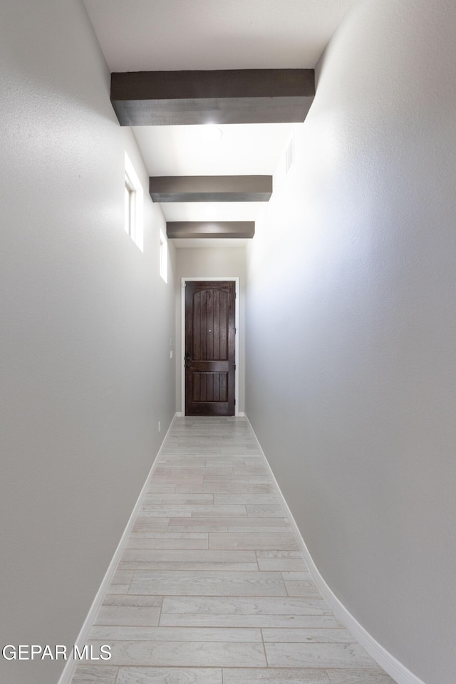 hall featuring light wood-type flooring, baseboards, and beamed ceiling