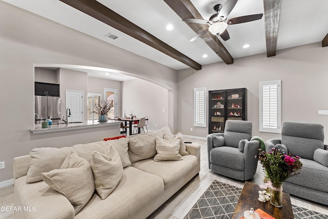 living room featuring arched walkways, recessed lighting, beam ceiling, and baseboards