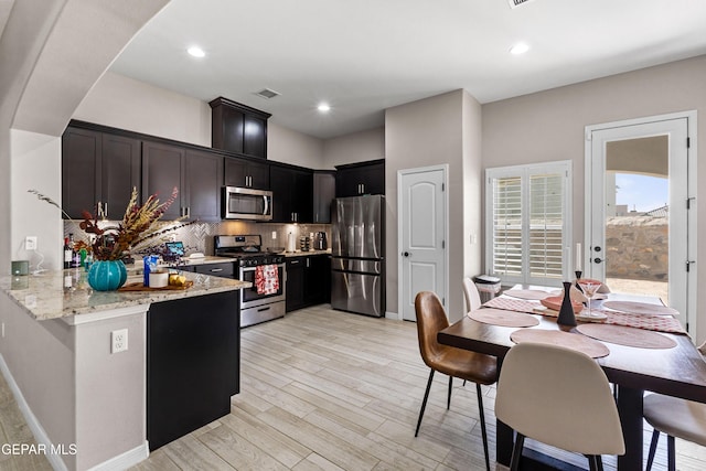 kitchen featuring visible vents, appliances with stainless steel finishes, light wood-type flooring, backsplash, and light stone countertops