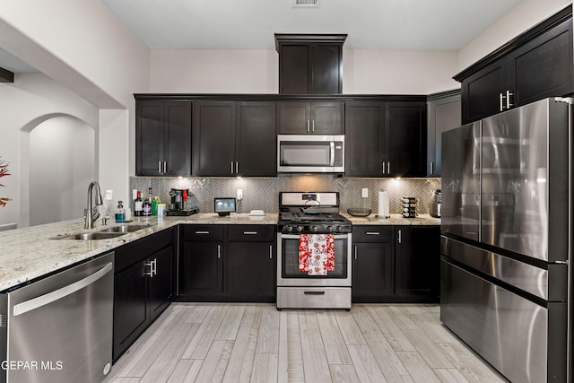 kitchen with stainless steel appliances, light stone counters, a sink, and tasteful backsplash