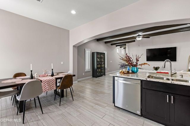 kitchen featuring arched walkways, dark cabinets, a sink, stainless steel dishwasher, and light wood finished floors