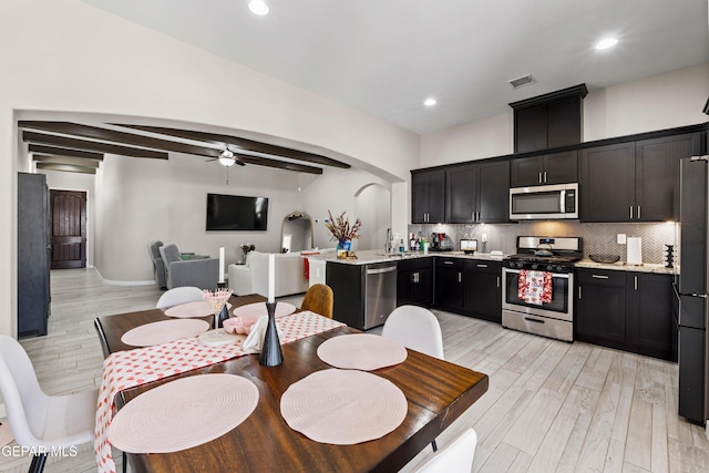 kitchen with arched walkways, light wood finished floors, stainless steel appliances, decorative backsplash, and a sink